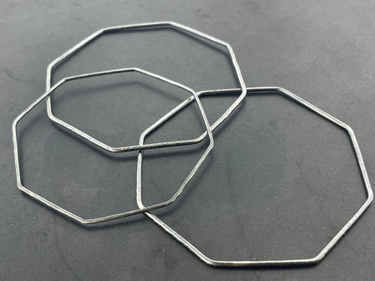 Three octagonal silver bangles on a dark gray background