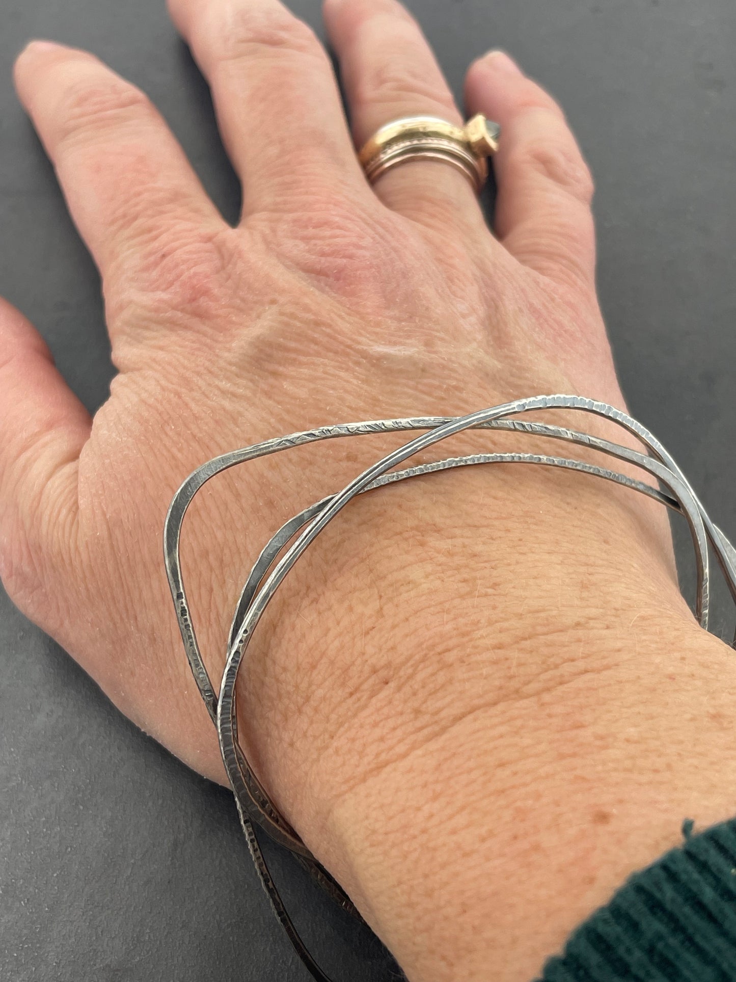Hand wearing multiple silver bracelets on a dark background