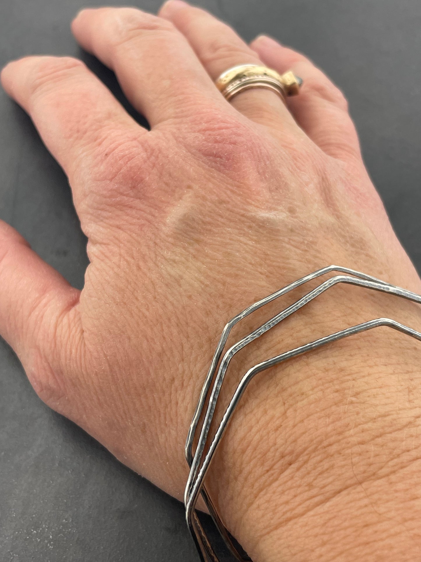 Hand wearing octagonal silver bracelets on a gray background