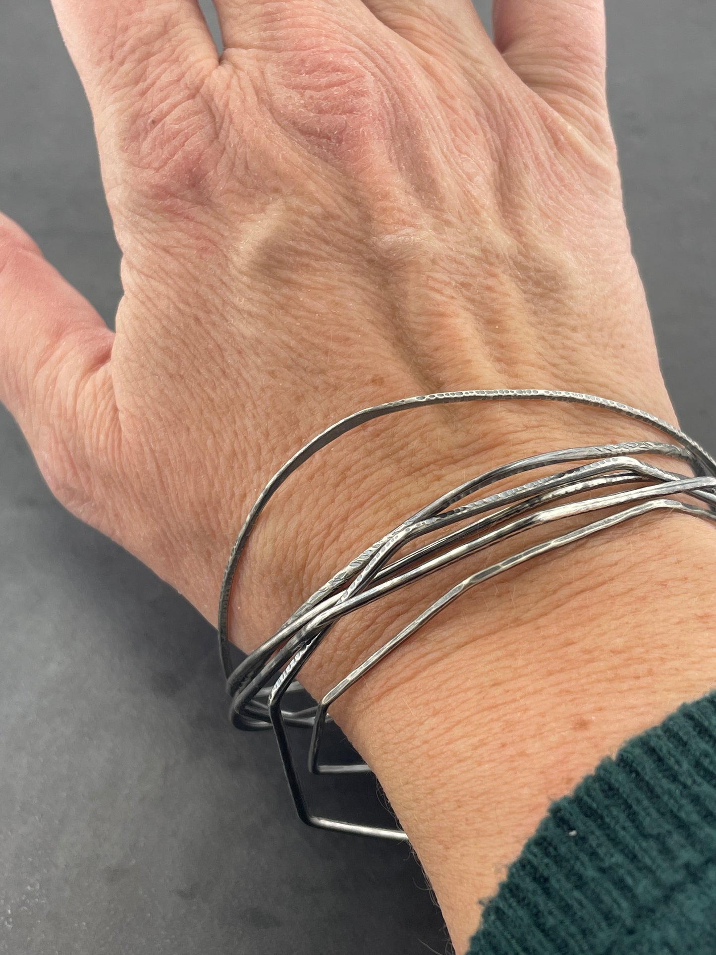 Hand wearing multiple silver bracelets on a dark background