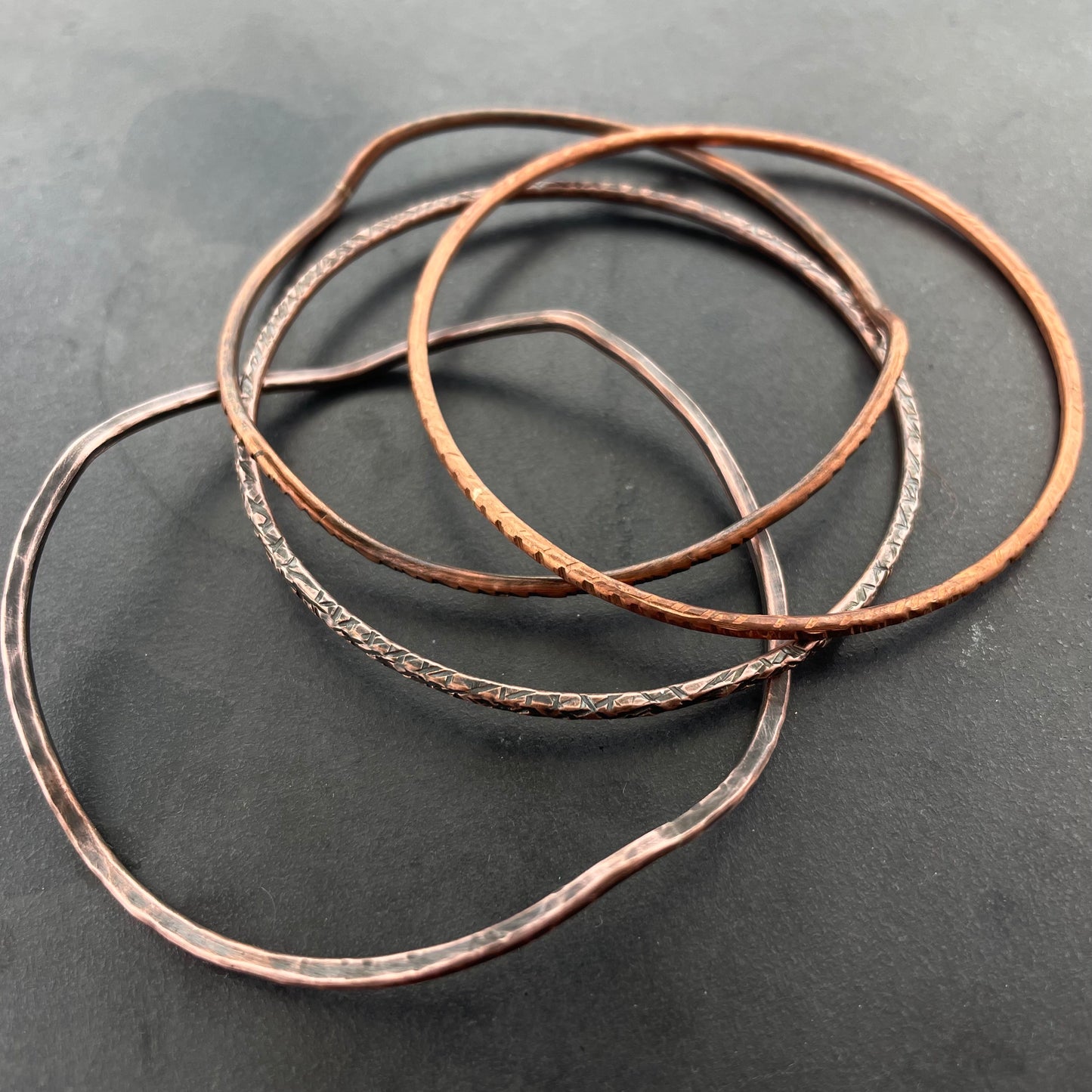 Three copper bracelets on a dark gray background