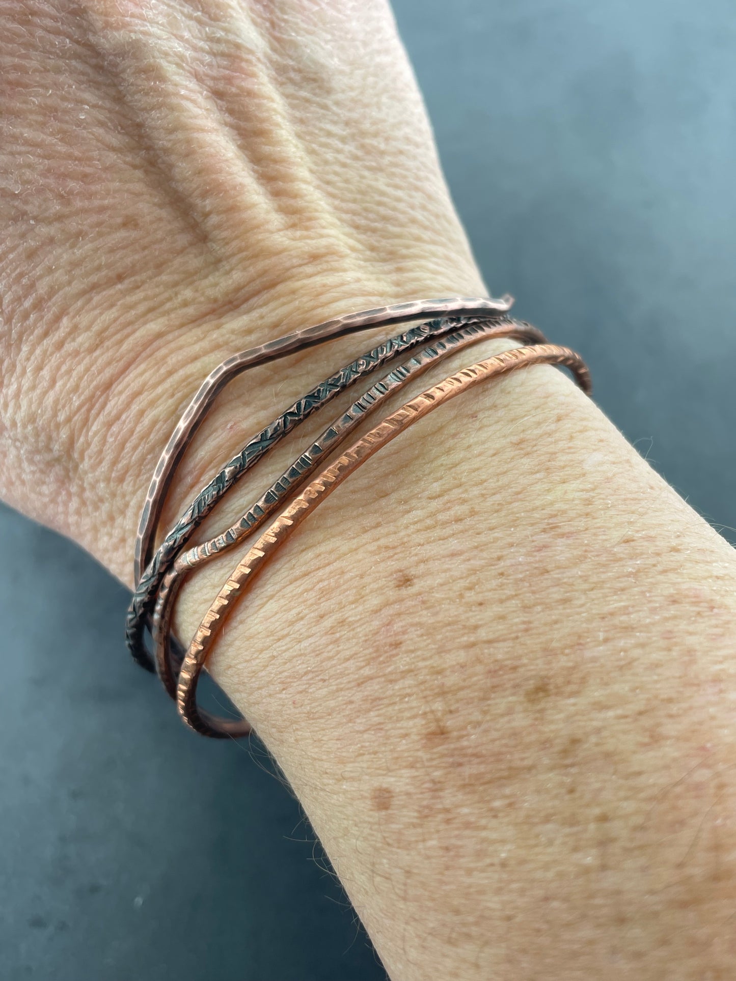 Close-up of a wrist wearing multiple thin bracelets on a neutral background
